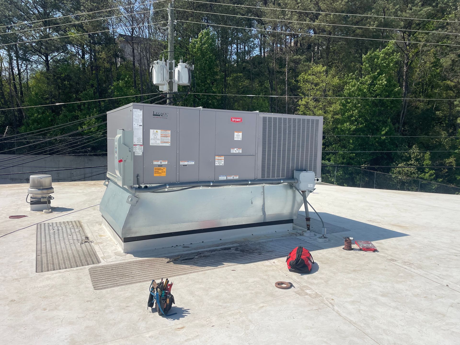 Rooftop HVAC unit with tools nearby; a sunny day with trees in the background.