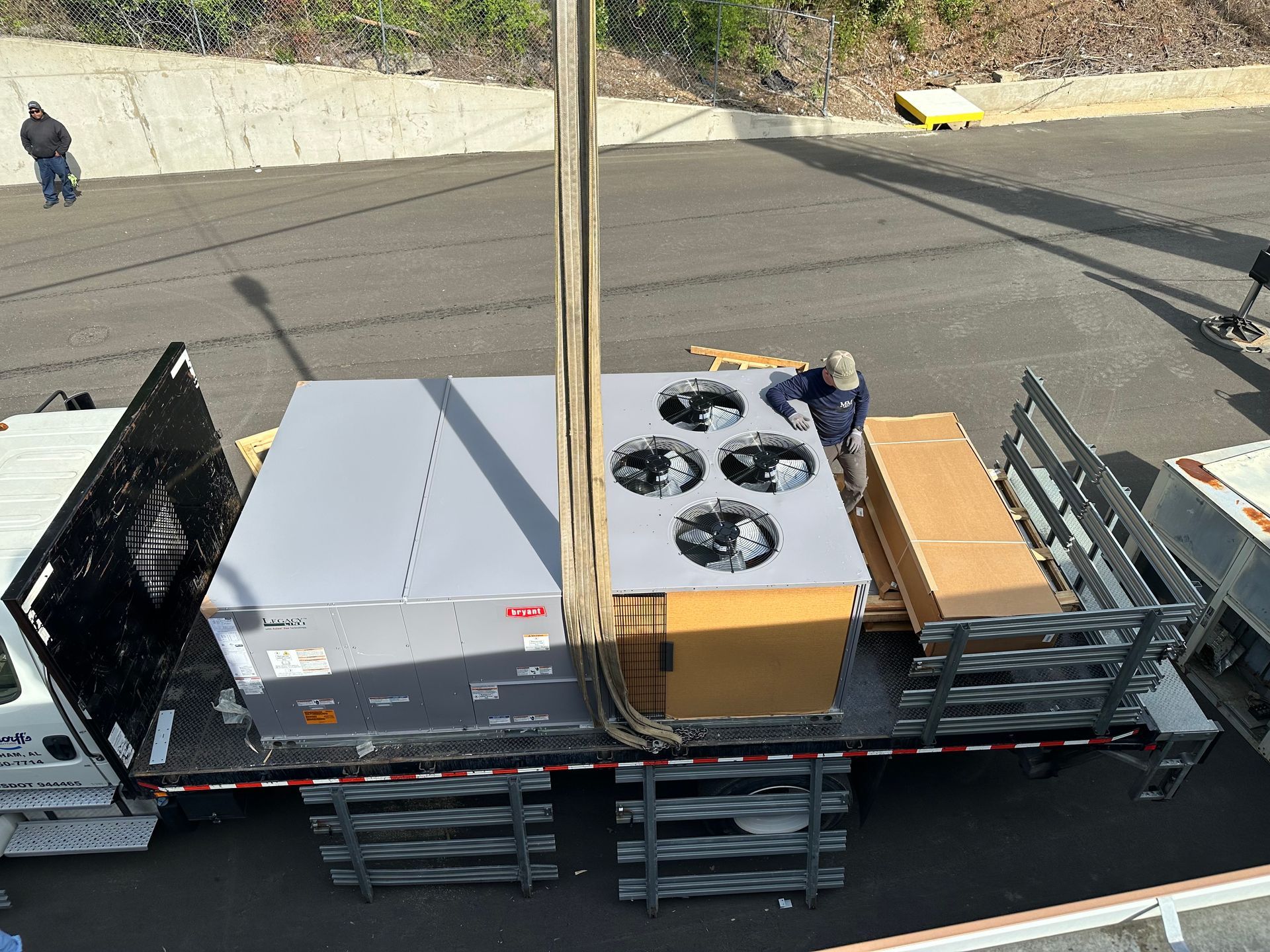 A large HVAC unit being lifted by a crane from a flatbed truck in an outdoor setting.