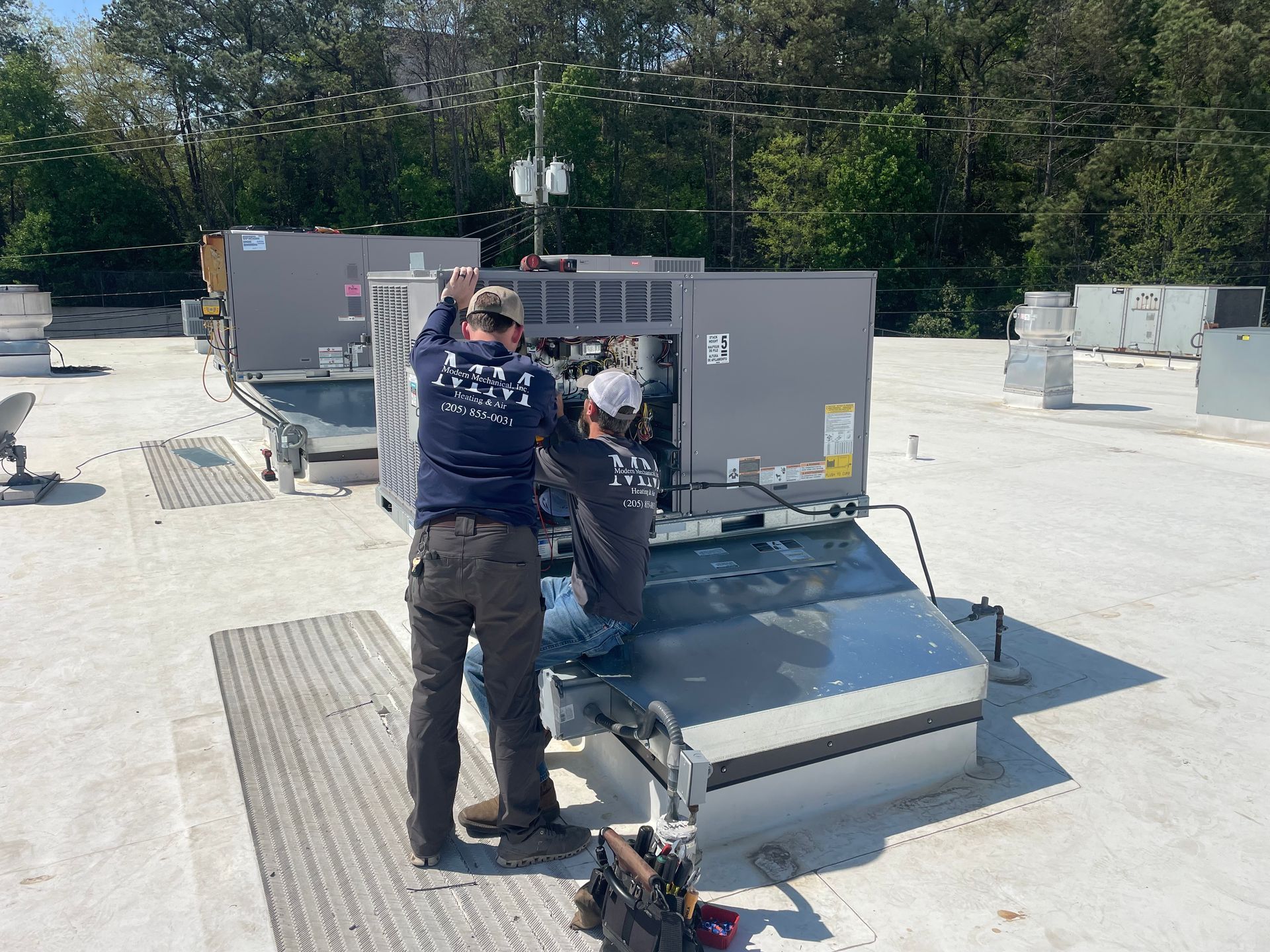 Two HVAC technicians working on rooftop air conditioning units.