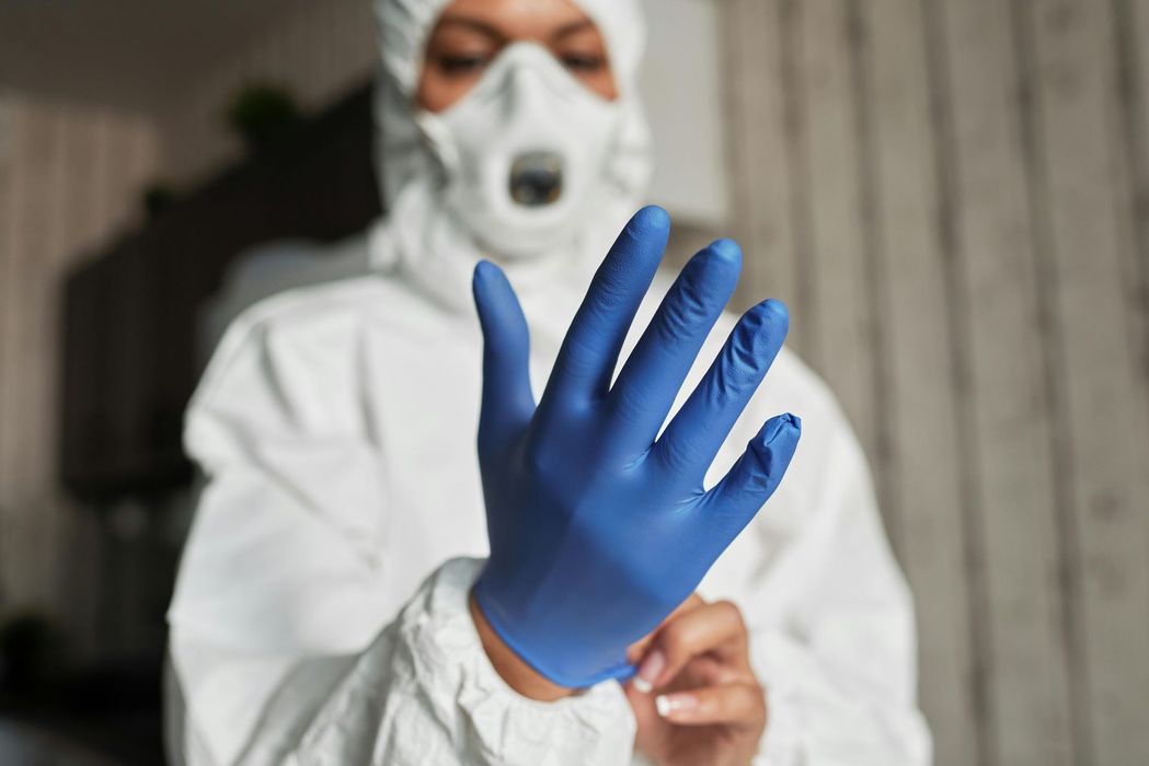 Person in hazmat suit putting on blue gloves.
