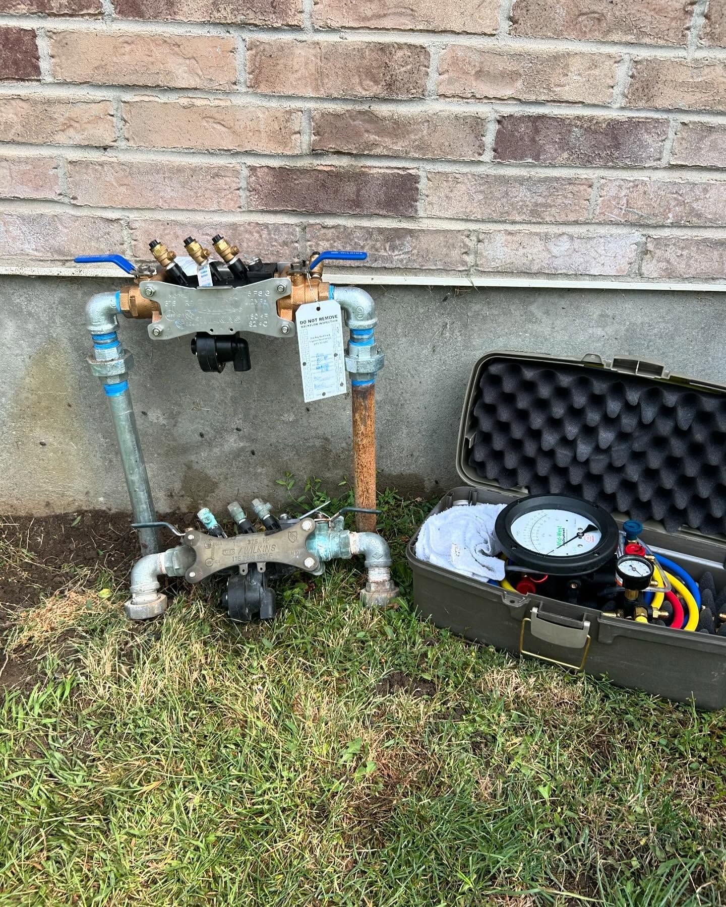A water meter is sitting on the grass next to a brick wall.