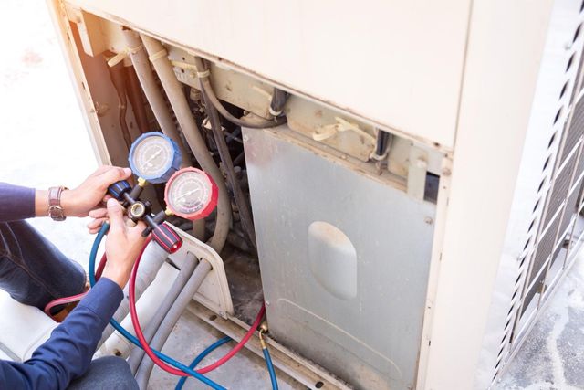 Person using gauges to service an outdoor air conditioning unit.
