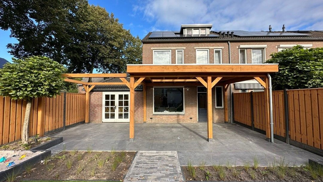 Een bakstenen huis met een houten pergola in de achtertuin.