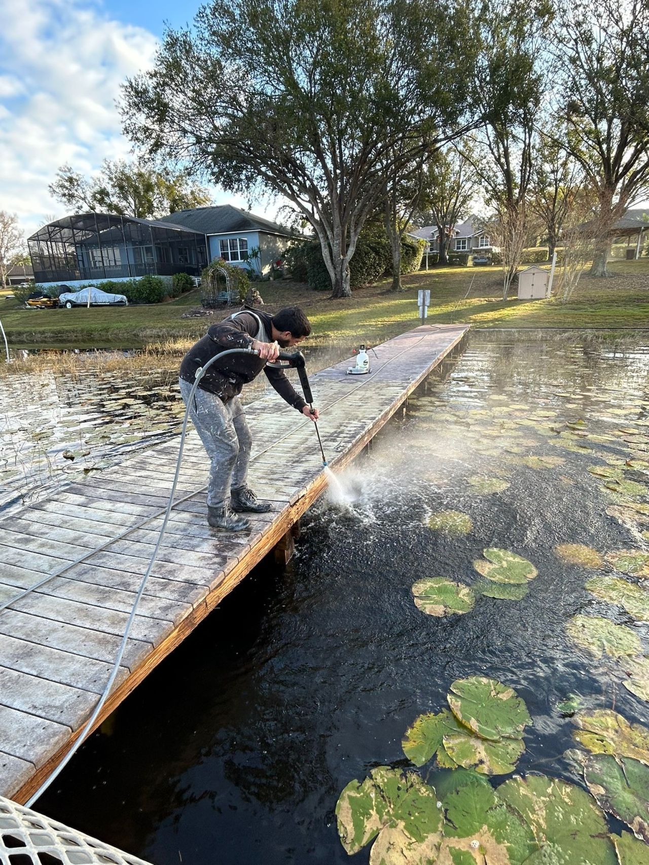 A man is cleaning a wooden dock with a high pressure washer.