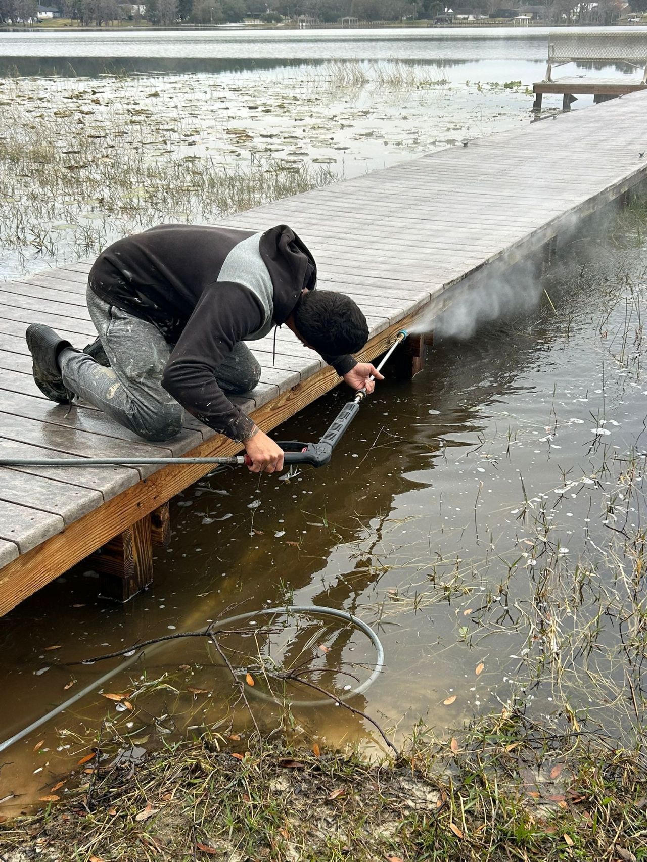 A man is kneeling on a wooden dock near a lake.