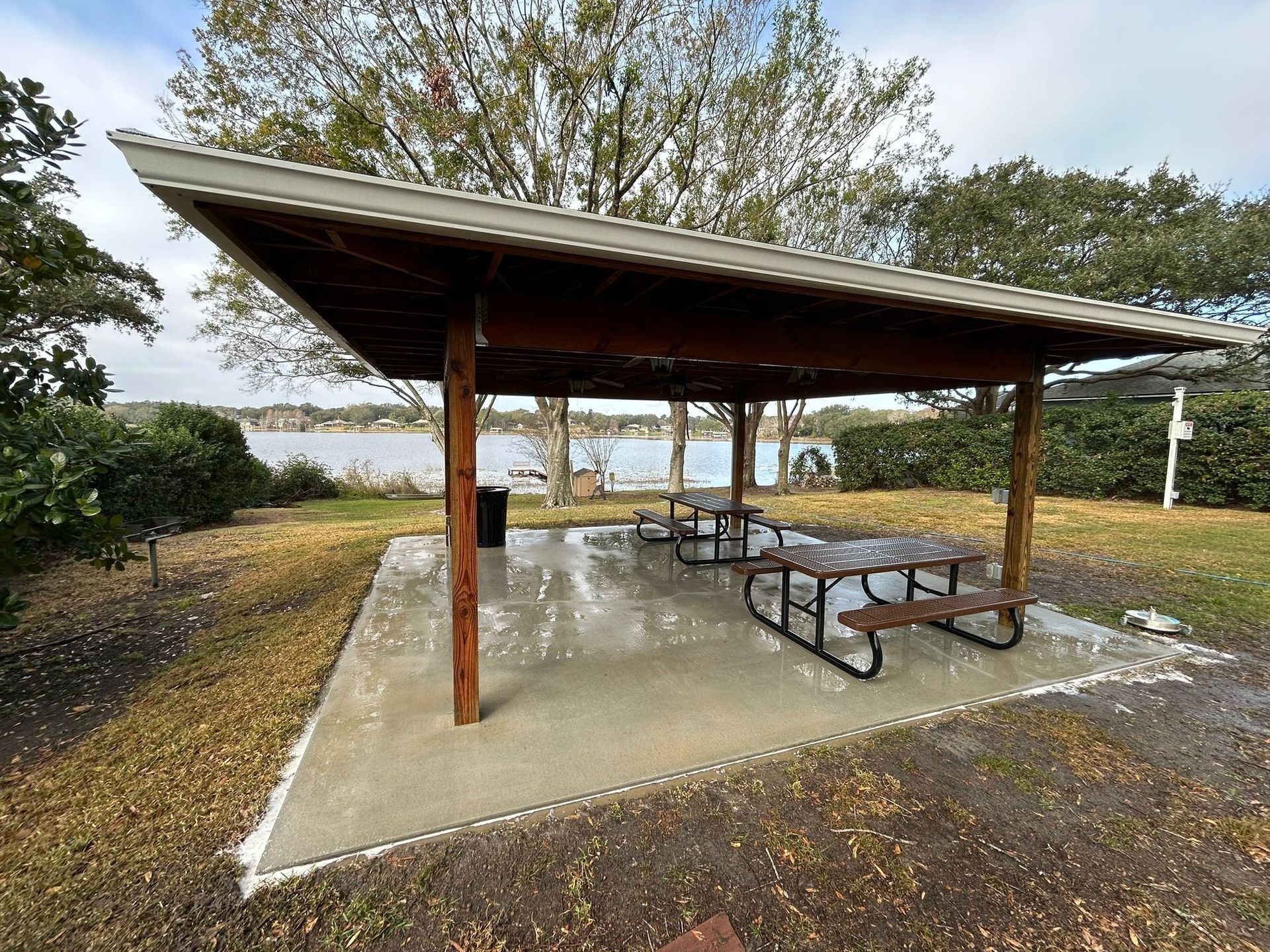 A picnic area with tables under a covered shelter next to a lake.