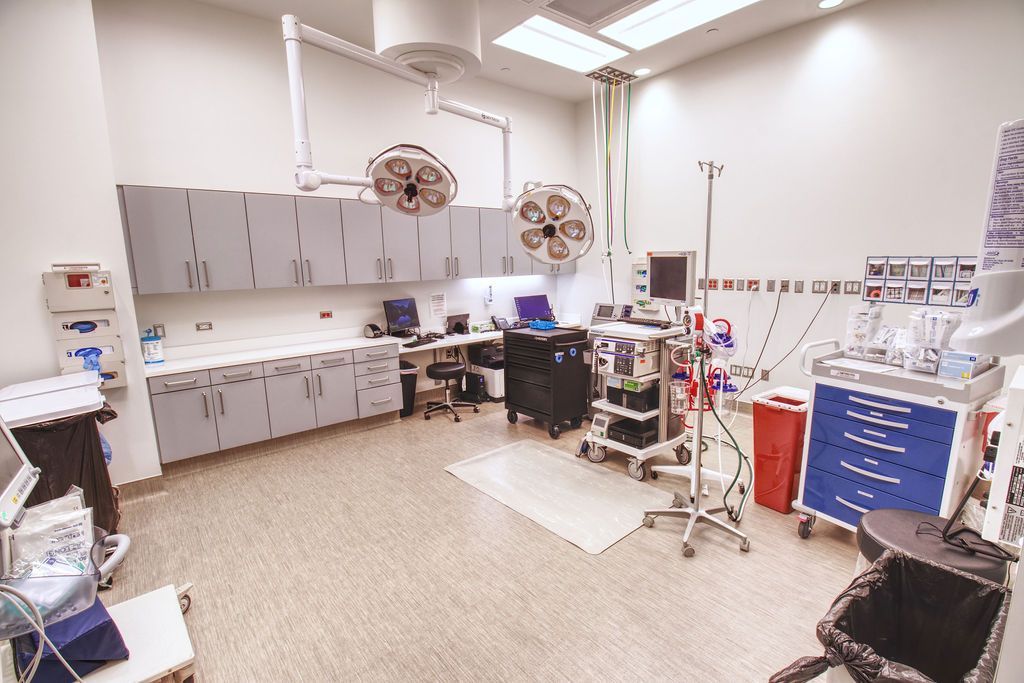 operating room show with two dome lights in the middle, surrounded by medical equipments, machine, monitors and computers.