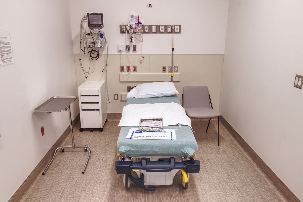 image of an emergency room cubicle with a bed in the middle surrounded by hospital equipments and a chair.