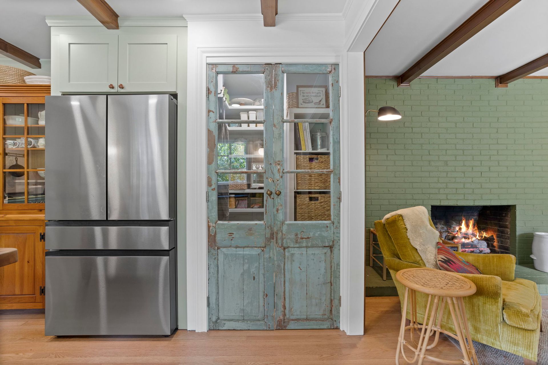 Refrigerator beside blue pantry doors, adjacent to a green brick fireplace and yellow chair.