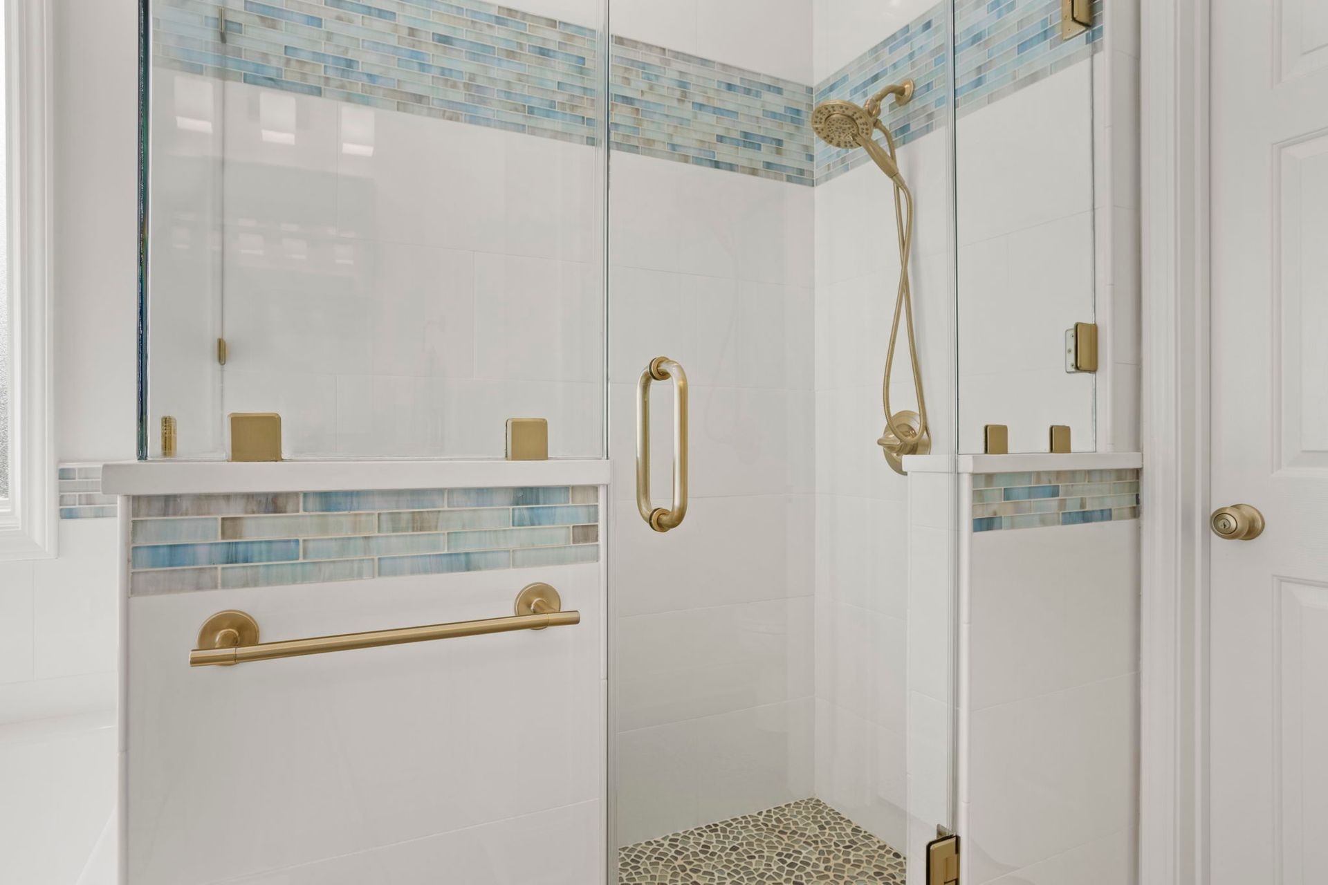 Glass shower with gold fixtures and blue tile accents remodeled by Nunley Custom Homes in Greenville, SC.
