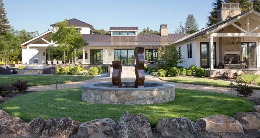Large house with a modern fountain in the foreground, surrounded by landscaping and lawn.