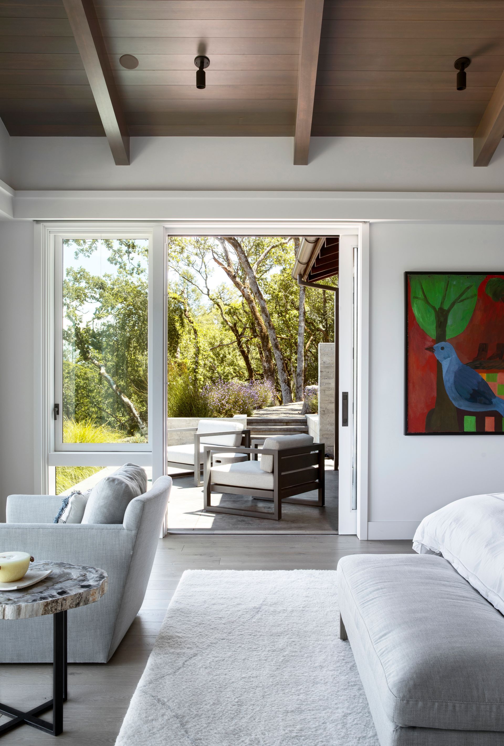 Bedroom with open sliding doors to a patio, gray furniture, and colorful bird art.