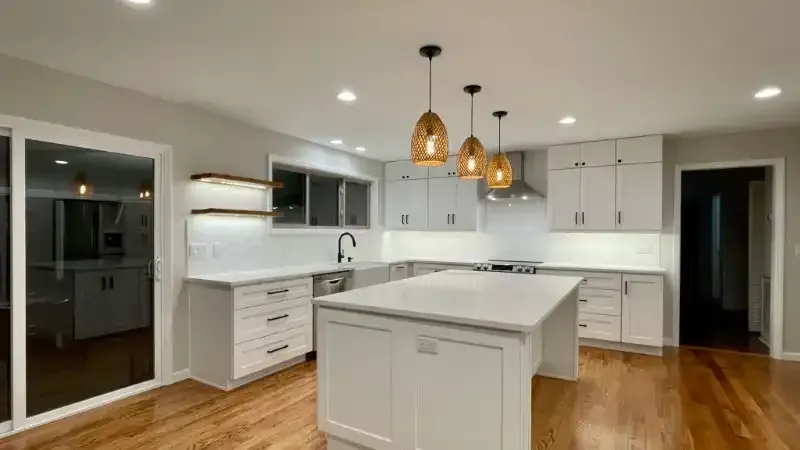 Modern white kitchen with island, pendant lights, and wood floors.