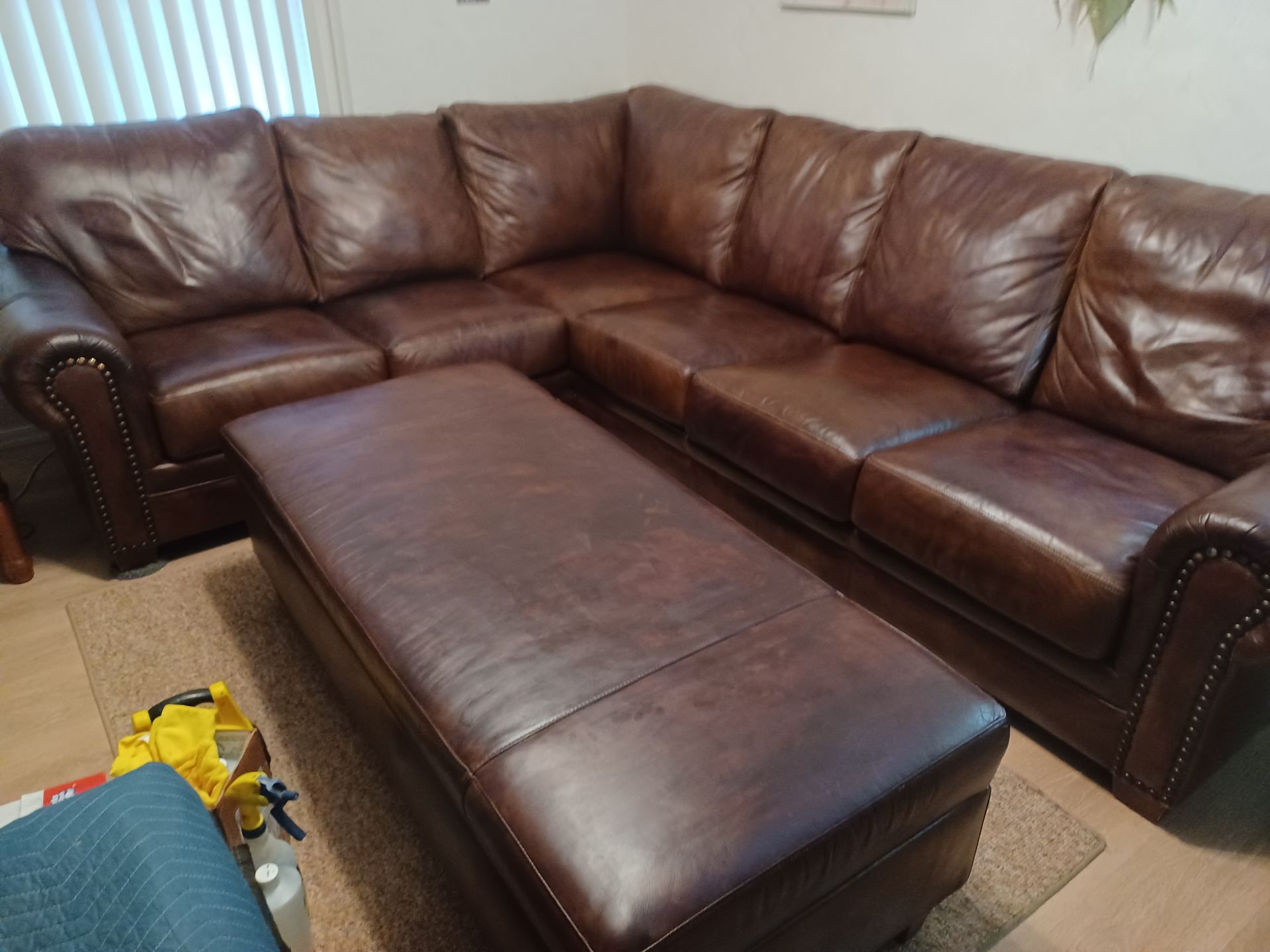 A brown leather sectional couch with an ottoman in a living room.