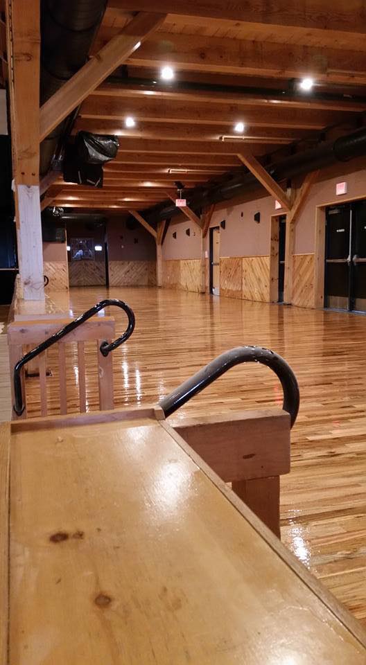 Empty venue with wood floor, ceiling beams, and bar. Railing in foreground.