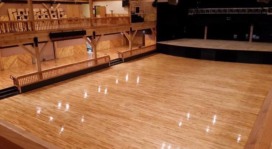 Empty wooden dance floor, stage, and balcony inside a large venue, possibly a ballroom.