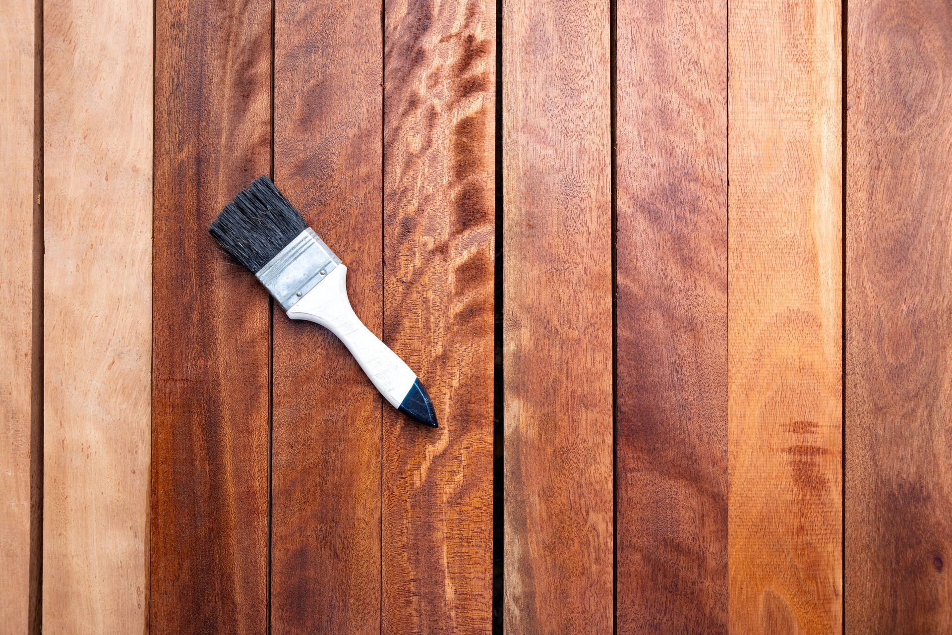 A paint brush rests on a freshly stained hardwood plank surface