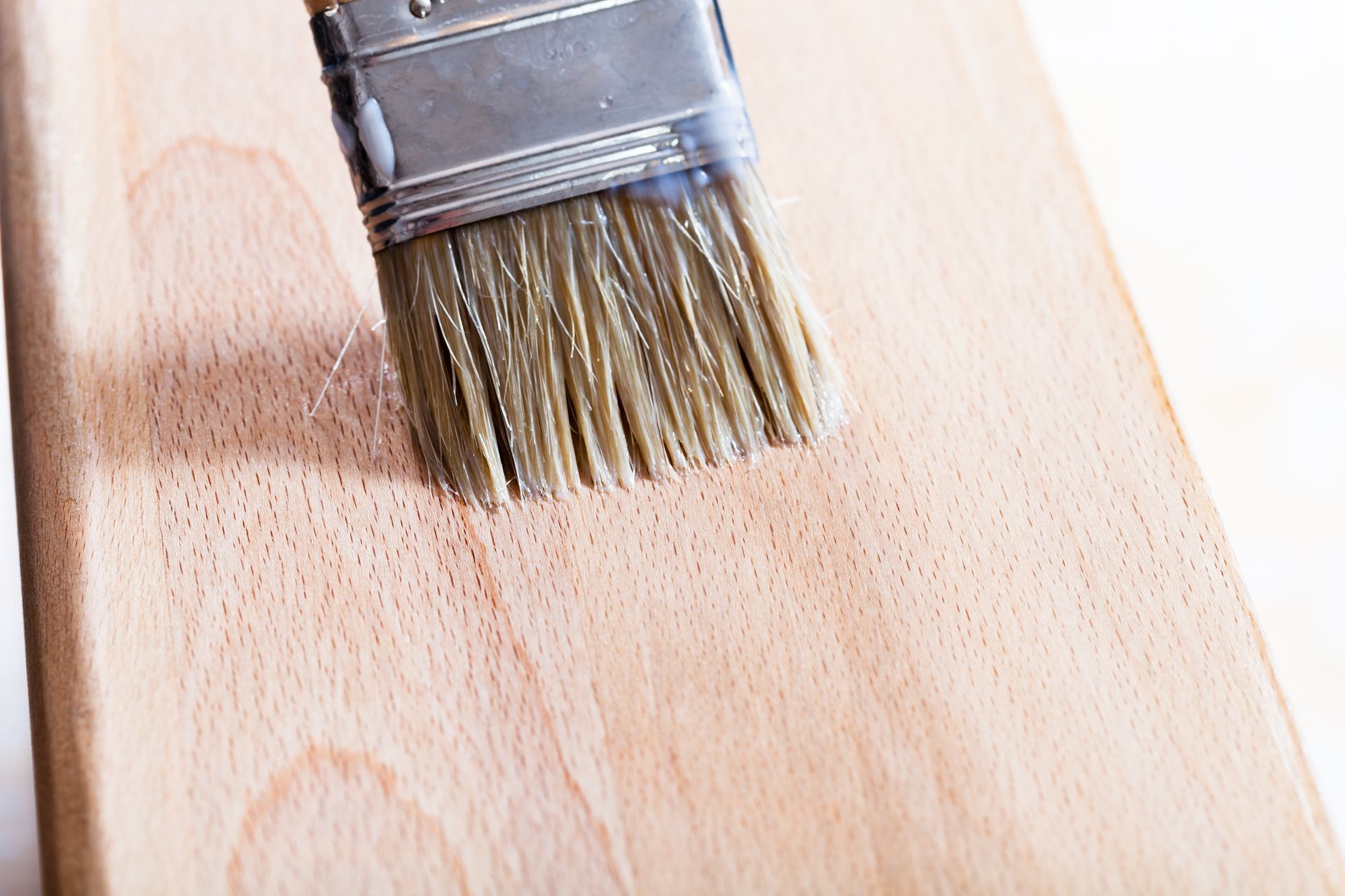 Applying clear wood finish on hardwood floor with a squeegee for smooth surface.