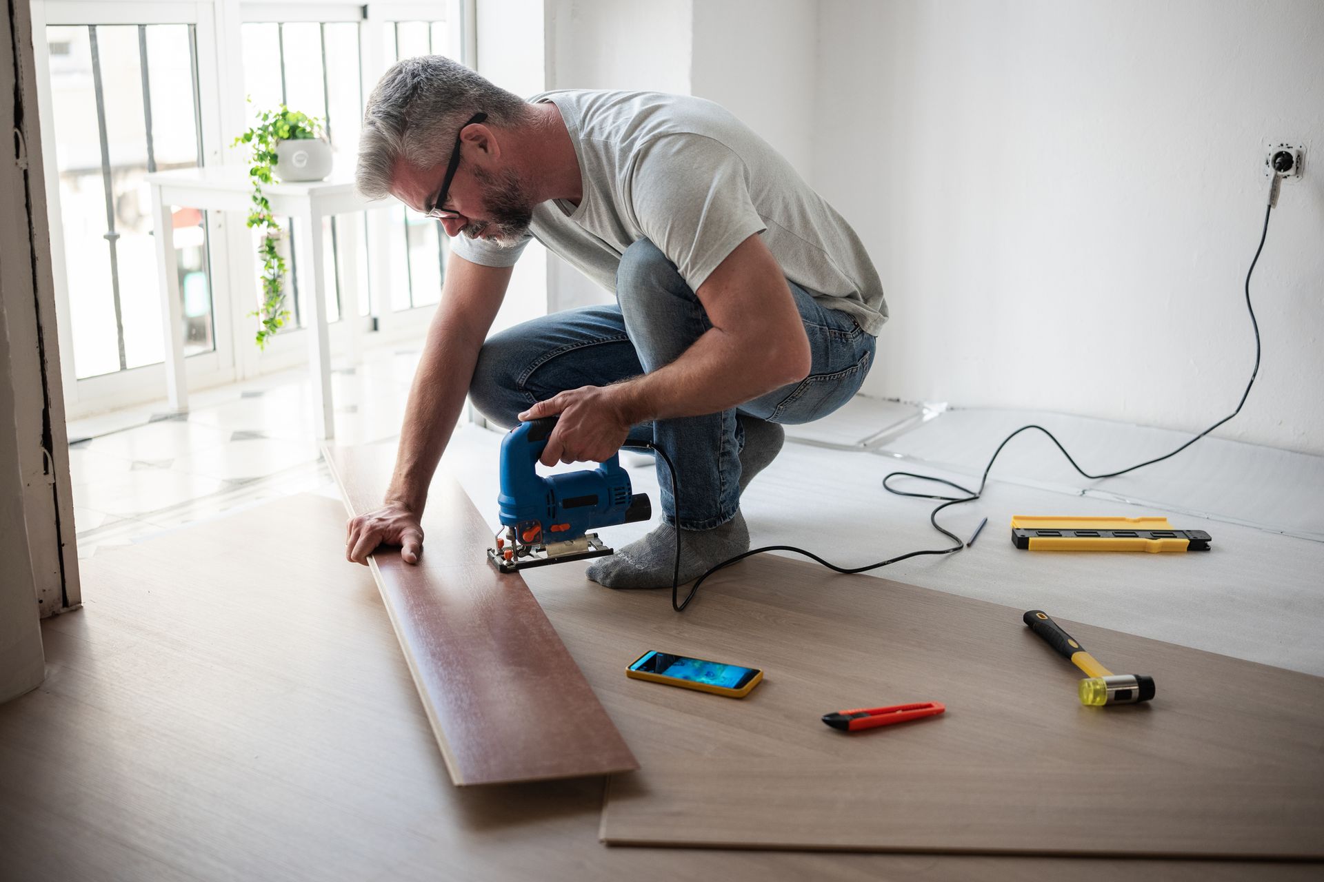 Carpenter cutting laminate floor plank using jigsaw, highlighting flooring services.