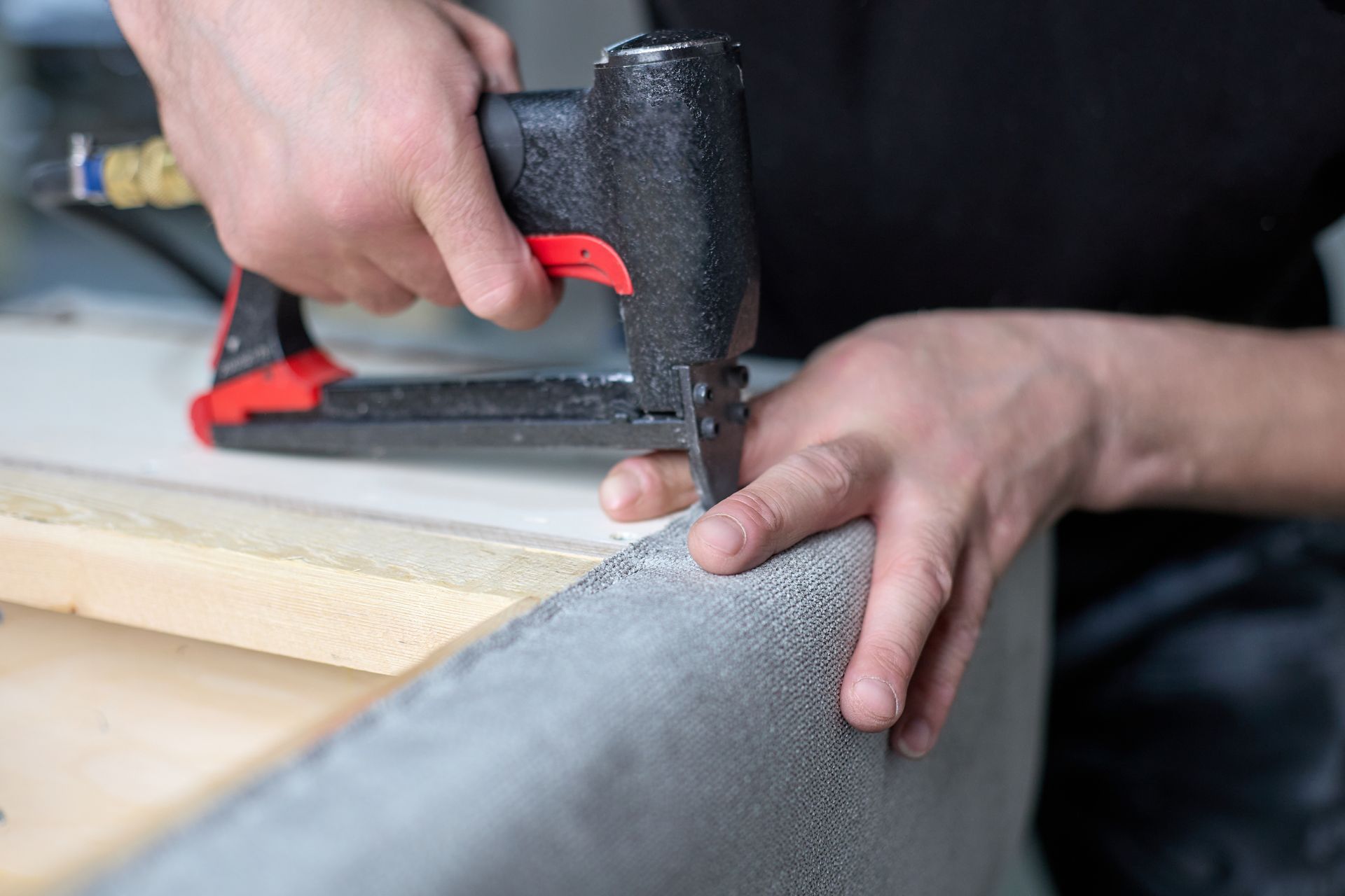 An upholstery repair shop worker using a staple gun to secure fabric on a furniture frame.