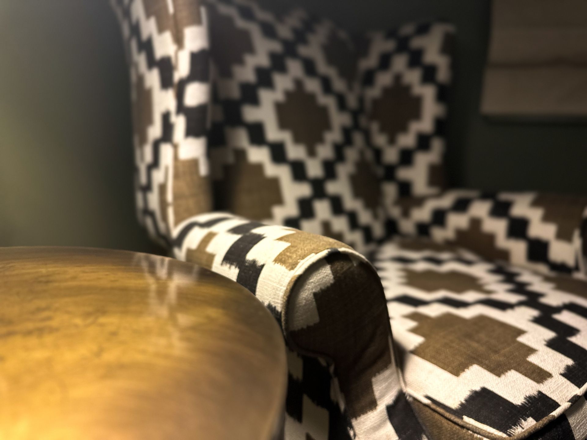 Armchair with bold geometric upholstery beside a wooden table in a warmly lit room. Armchair with bold geometric upholstery beside a wooden table in a warmly lit room.