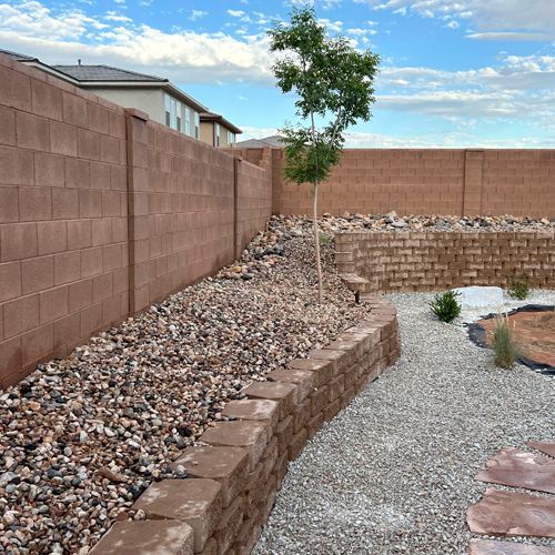 A brick wall surrounds a gravel area in a backyard.