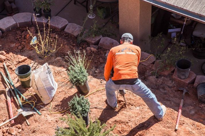 A man in an orange shirt is kneeling down in the dirt.
