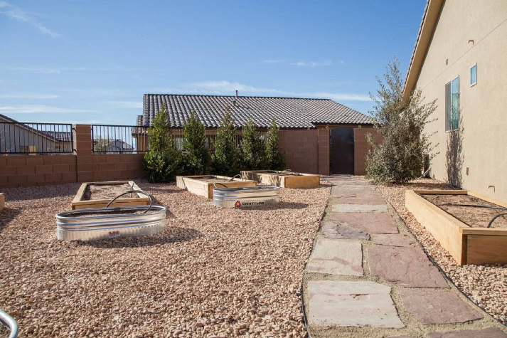 A brick walkway leading to a house with a lot of raised beds.