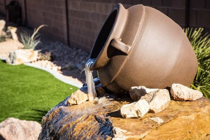 A pot with water pouring out of it is sitting on top of a rock.