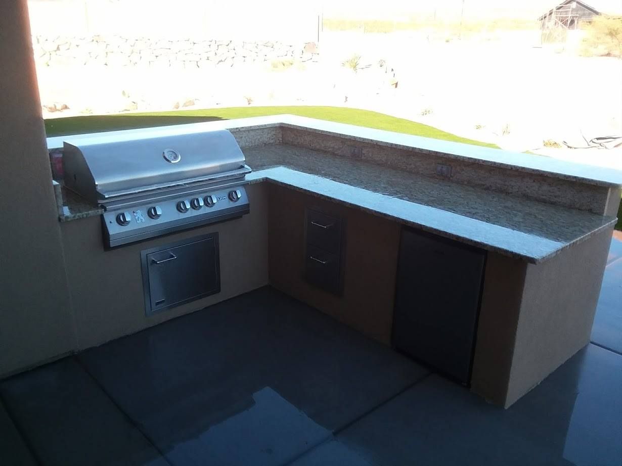 An outdoor kitchen with a grill and granite counter tops
