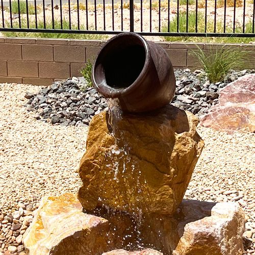 A garden with rocks , plants and flowers in front of a house.