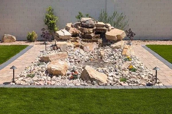 Water fountain feature in a backyard with large rocks, flowing water, and surrounding landscaping.