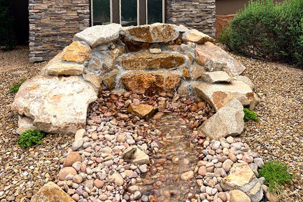 A waterfall made of rocks in front of a house.