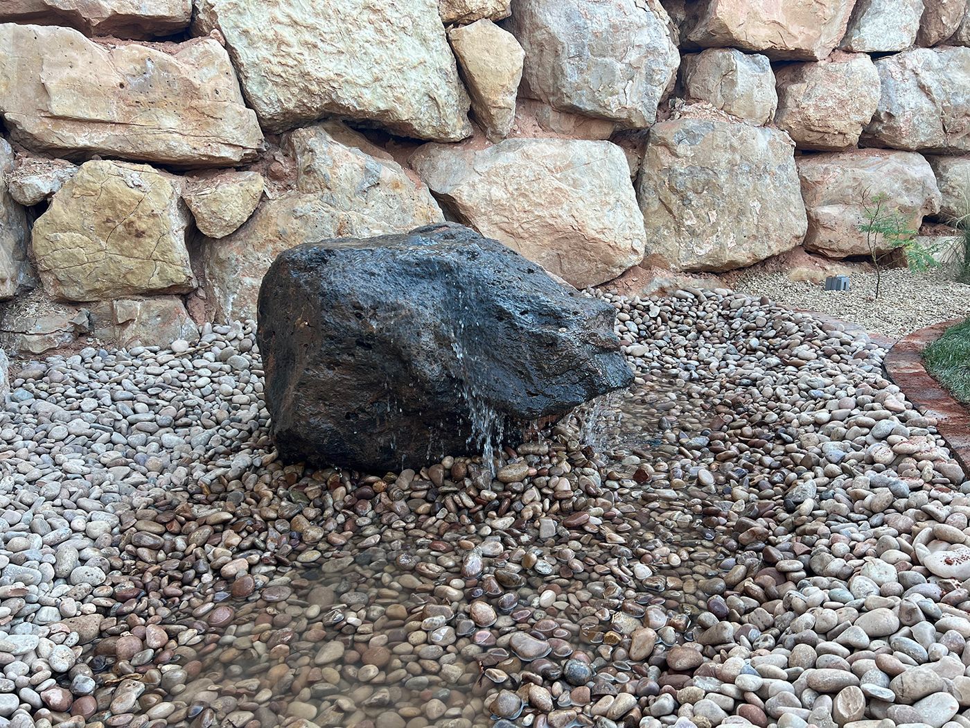 A large rock is sitting on top of a pile of gravel in front of a stone wall.