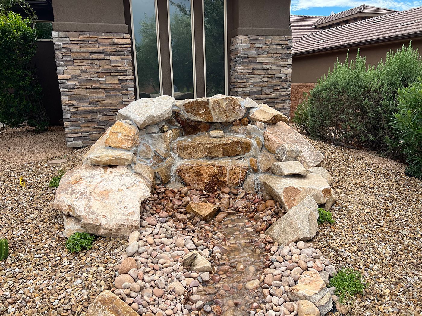 A waterfall is surrounded by rocks and gravel in front of a house.