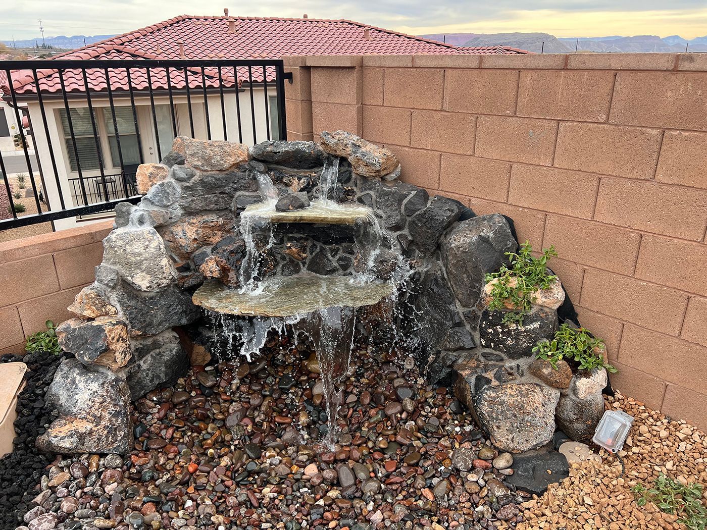A waterfall is surrounded by rocks and a brick wall.