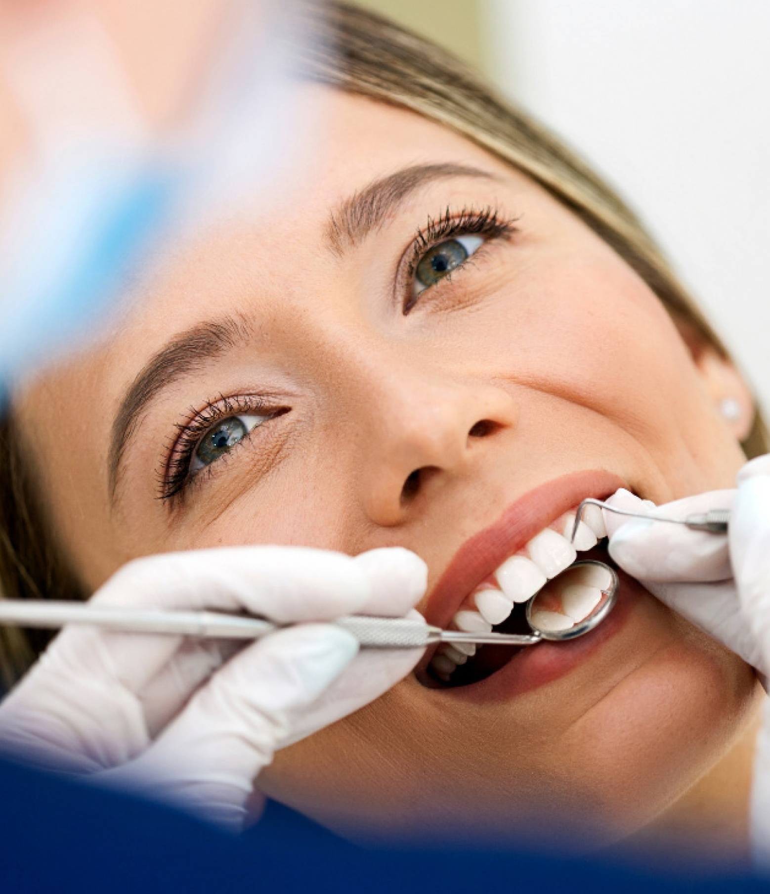 Woman at dentist appointment with tools in her mouth, smiling.