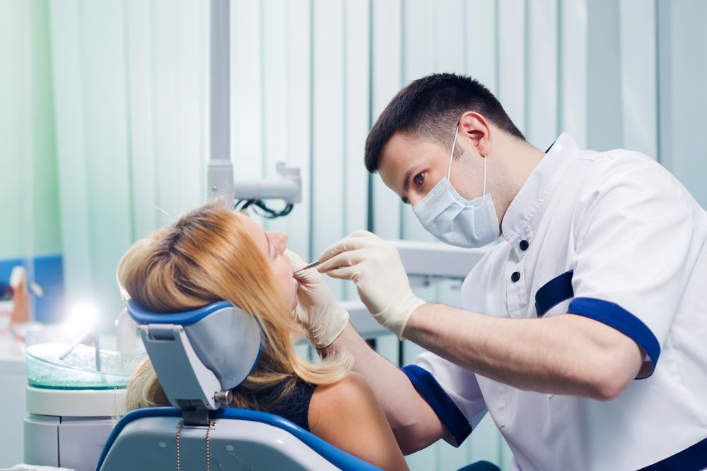 A woman is sitting in a dental chair while a dentist examines her teeth.