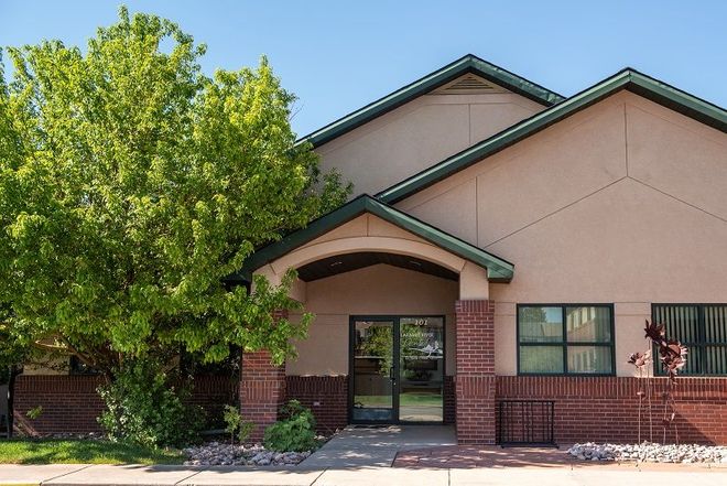 Building entrance with brick accents, arched doorway, and a tree on the left under a blue sky.