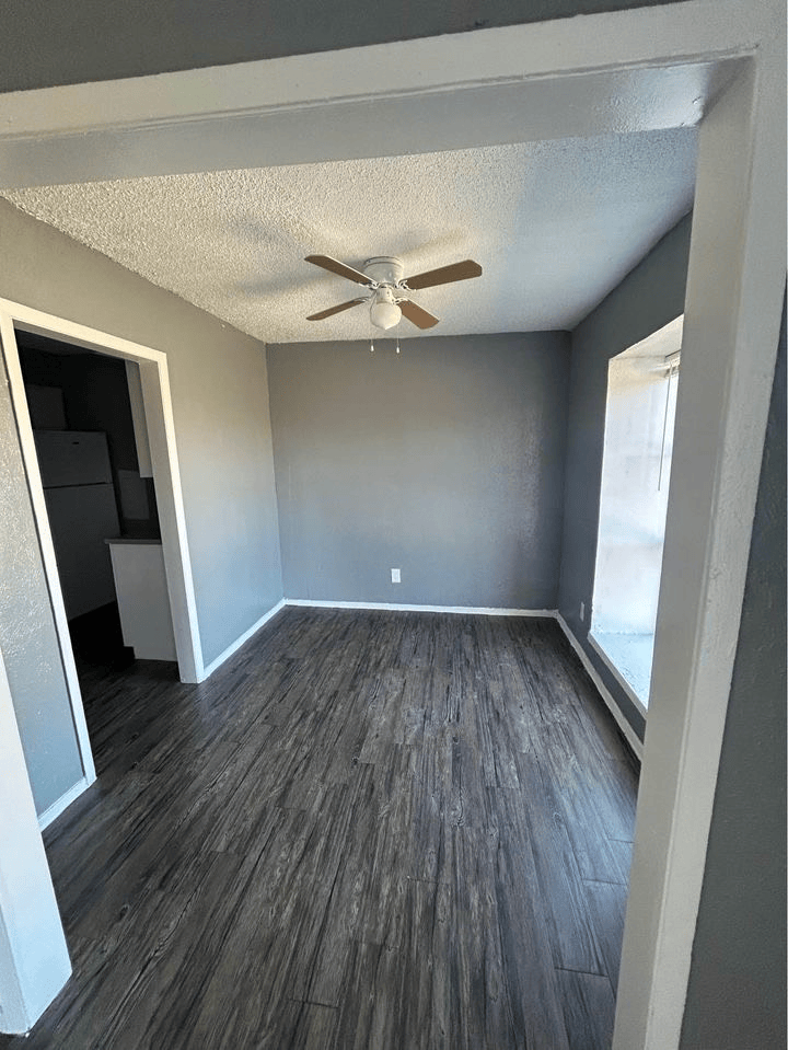 Gray-painted room with dark wood-look flooring, a ceiling fan, and a doorway to the kitchen.