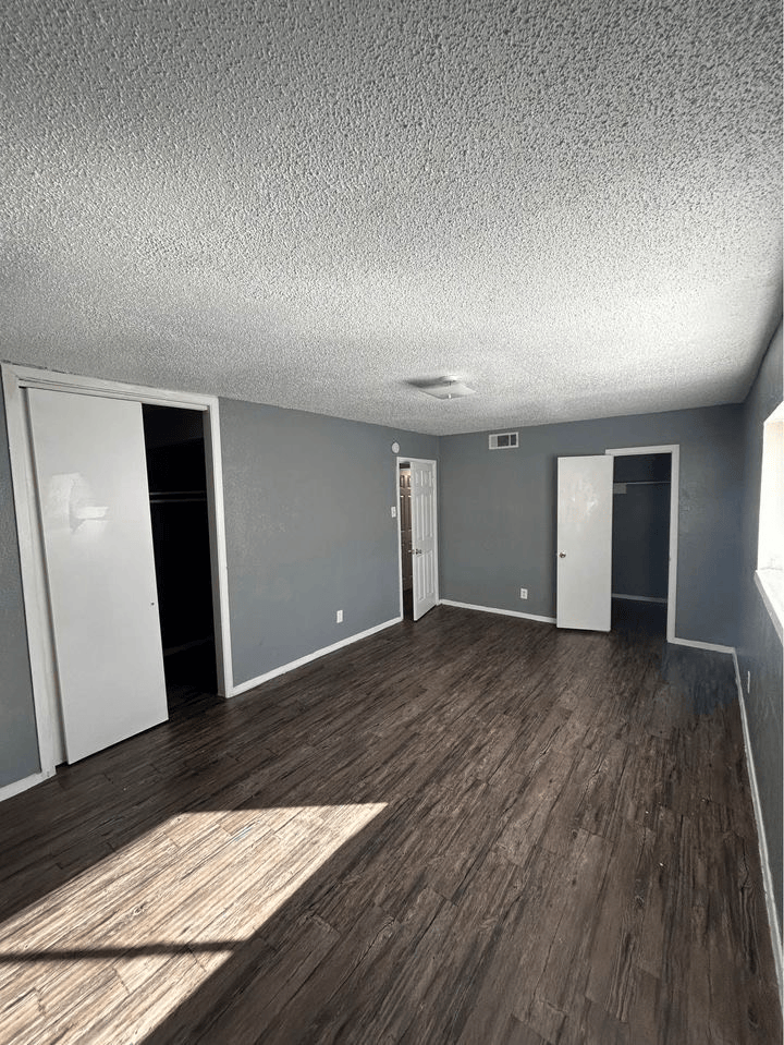 Empty bedroom with gray walls, dark wood-look floor, white doors, and textured ceiling.