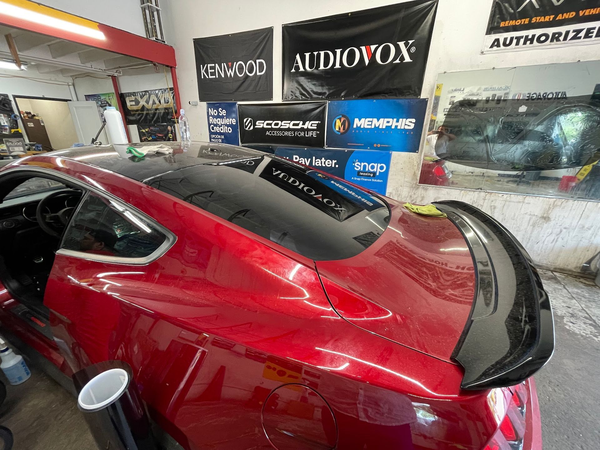 Red sports car with black spoiler and tinted windows, inside an auto shop.