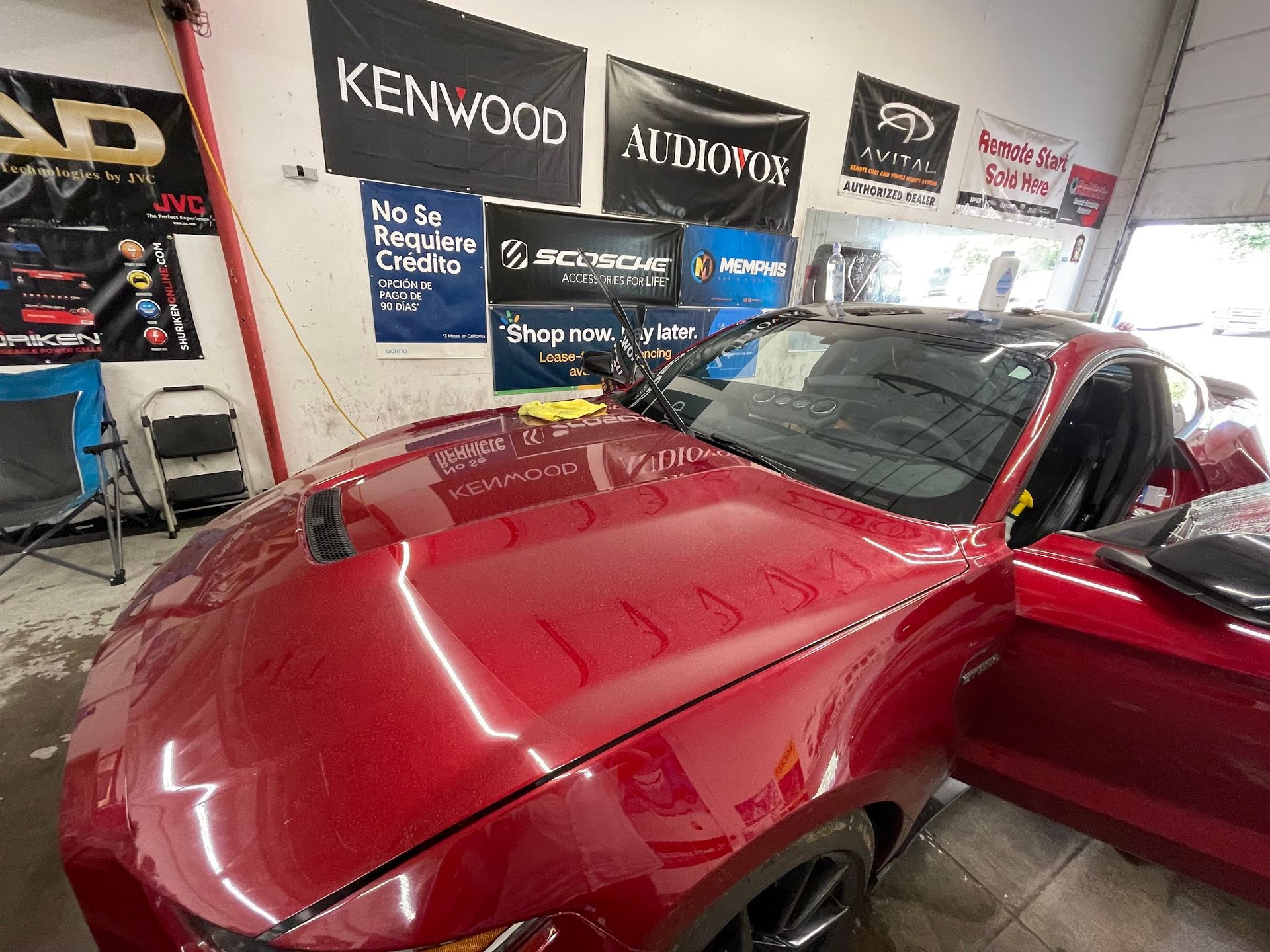 Red car being worked on inside a shop with branded flags and equipment. Open door.