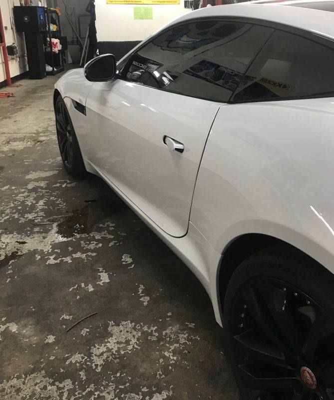 White Jaguar sports car parked in a garage with black wheels and tinted windows.