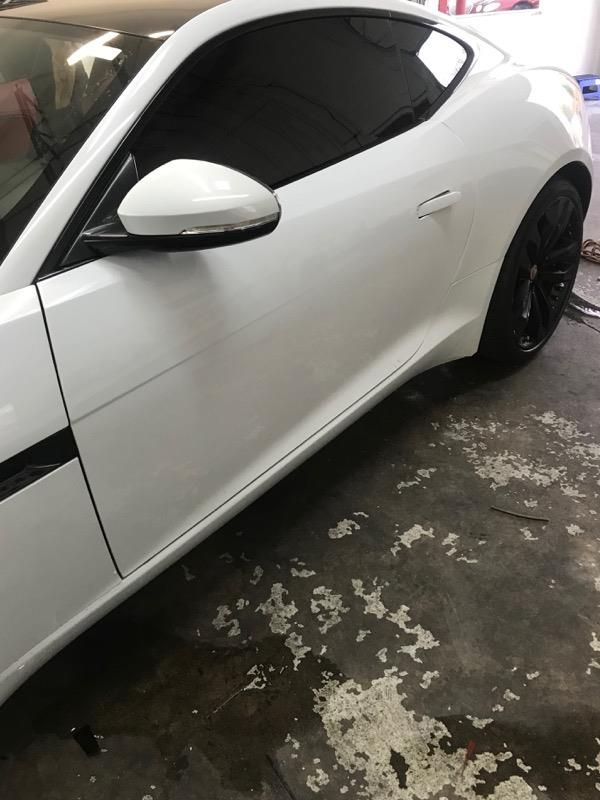 White Jaguar sports car, side view, tinted windows, black rims, parked in garage.