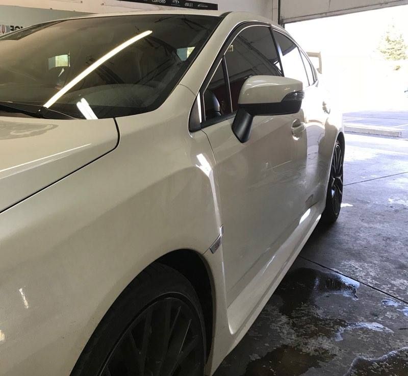White Subaru car with black wheels parked in a garage.
