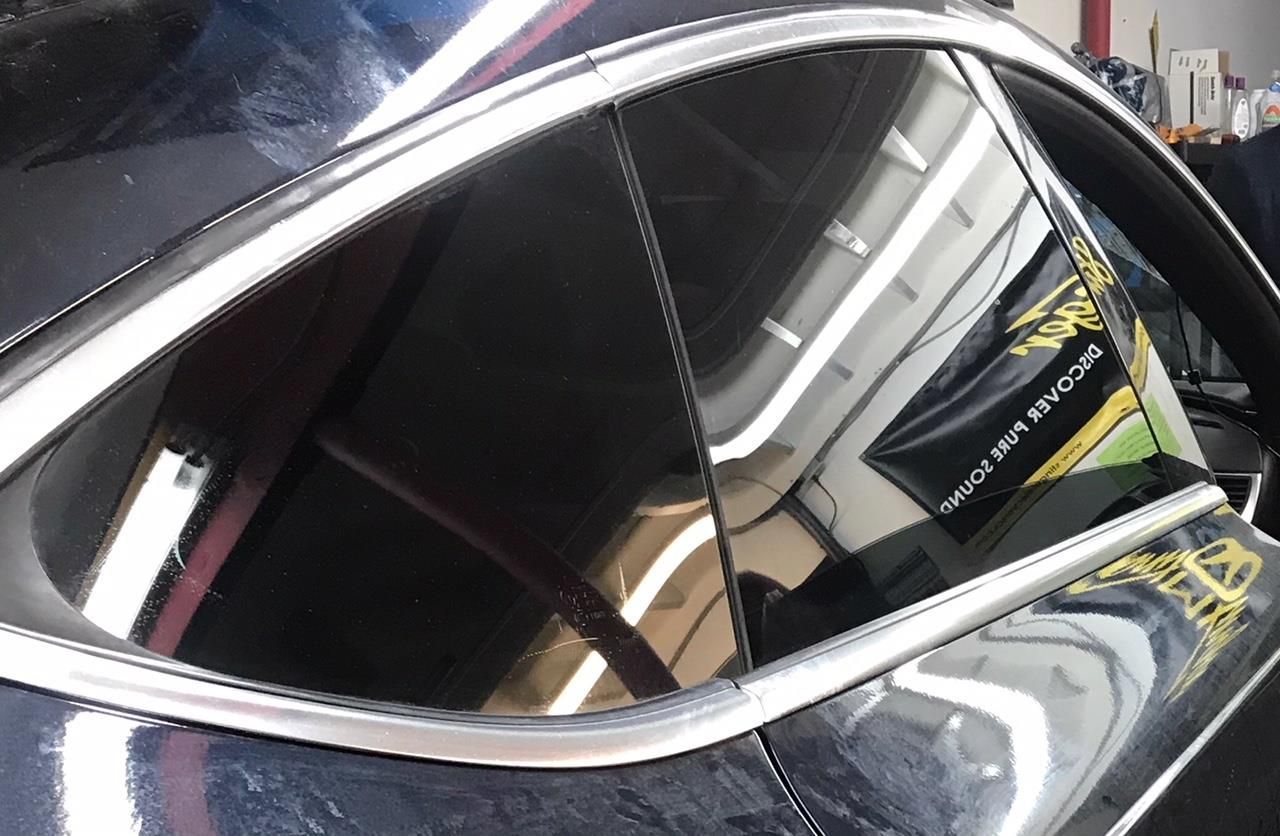 Close-up of a dark-tinted car window with a silver trim, reflecting interior objects.