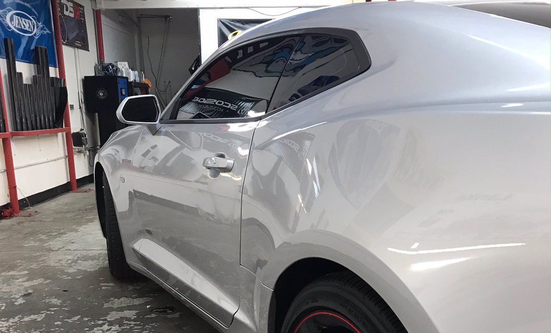 Silver car in a shop, side view, partially showing the door, wheel, and roof.