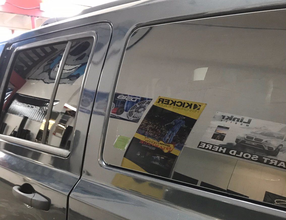 Dark gray SUV window reflecting a shop interior with posters.
