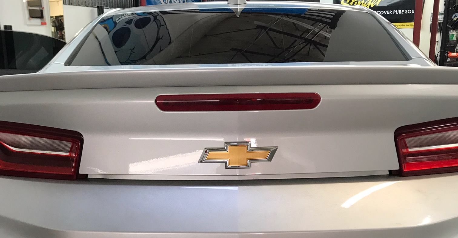 White Chevrolet Camaro's rear with tinted windows and a red brake light. The Chevy logo is visible.